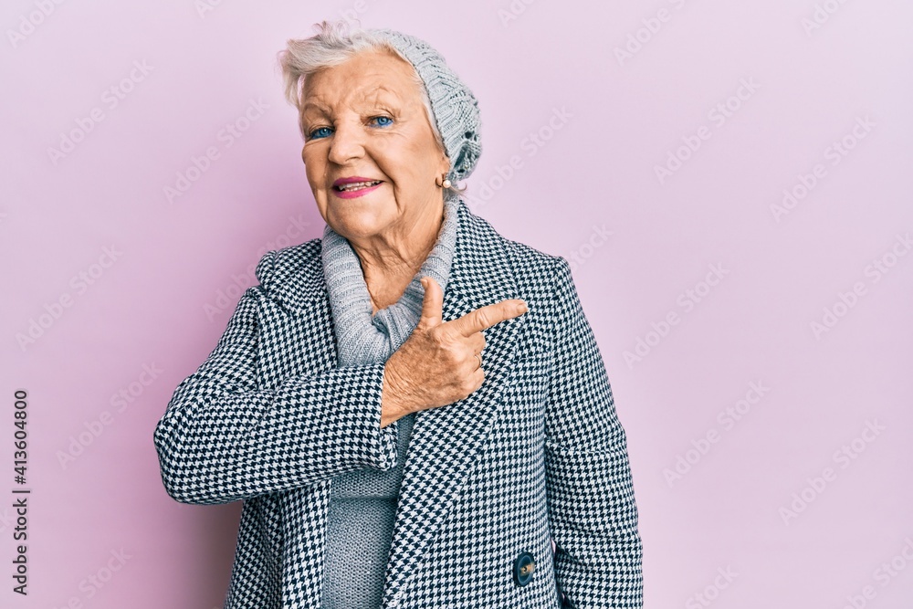 Senior grey-haired woman wearing wool winter sweater smiling cheerful pointing with hand and finger up to the side Senior grey-haired woman wearing wool winter sweater smiling cheerful pointing with hand and finger up to the side