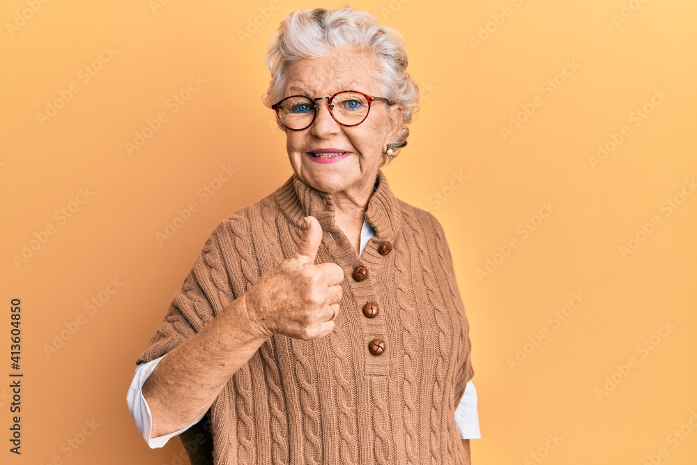 Senior grey-haired woman wearing casual clothes and glasses doing happy thumbs up gesture with hand. approving expression looking at the camera showing success. Senior grey-haired woman wearing casual clothes and glasses doing happy thumbs up gesture with hand. approving expression looking at the camera showing success.