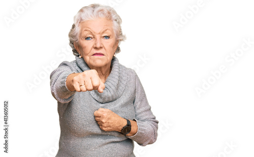 Fotografie, Obraz Senior grey-haired woman wearing casual winter sweater punching fist to fight, a