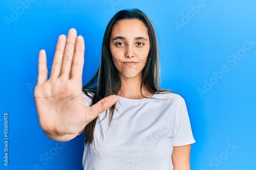 Young hispanic woman wearing casual white t shirt doing stop sing with palm of the hand. warning expression with negative and serious gesture on the face.