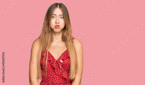 Beautiful blonde woman wearing summer dress puffing cheeks with funny face. mouth inflated with air, crazy expression.