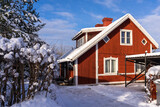 Traditional old red wooden houses in countryside. Decorative shrub around the house. Fence or hedge covered with snow in the foreground. Evergreen trees grow in the yard. Beautiful red cottage, villa.