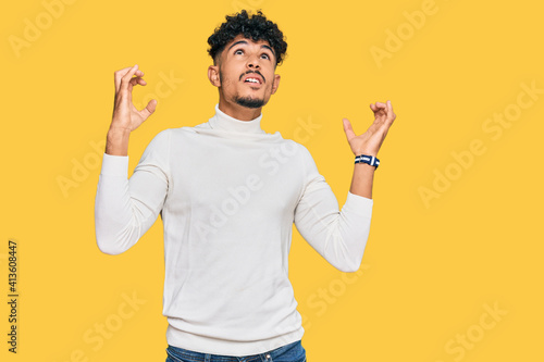 Young arab man wearing casual winter sweater crazy and mad shouting and yelling with aggressive expression and arms raised. frustration concept.