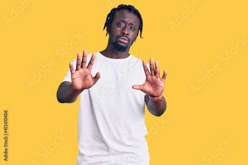 Young african american man with braids wearing casual white tshirt doing stop gesture with hands palms, angry and frustration expression