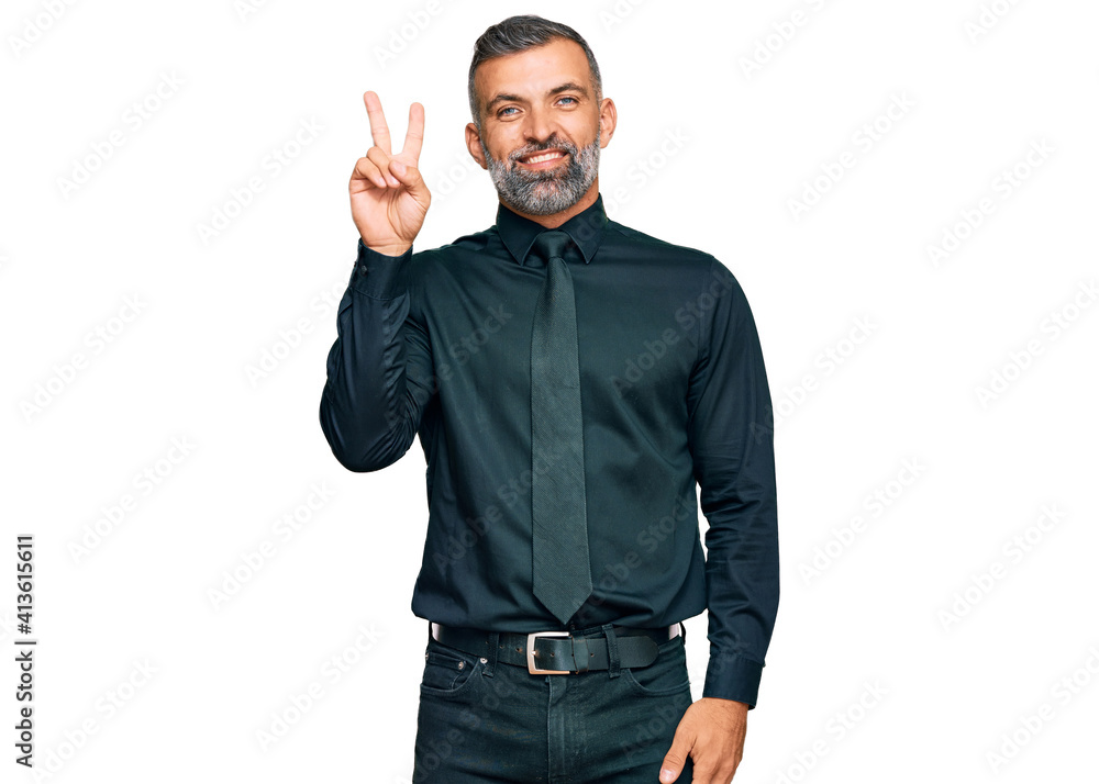 Fototapeta premium Middle age handsome man wearing business clothes smiling with happy face winking at the camera doing victory sign. number two.