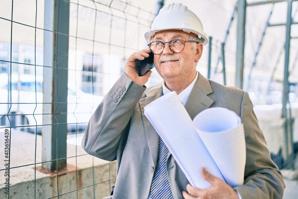 Senior grey-haired architect man holding blueprints using smartphone at street of city Senior grey-haired architect man holding blueprints using smartphone at street of city