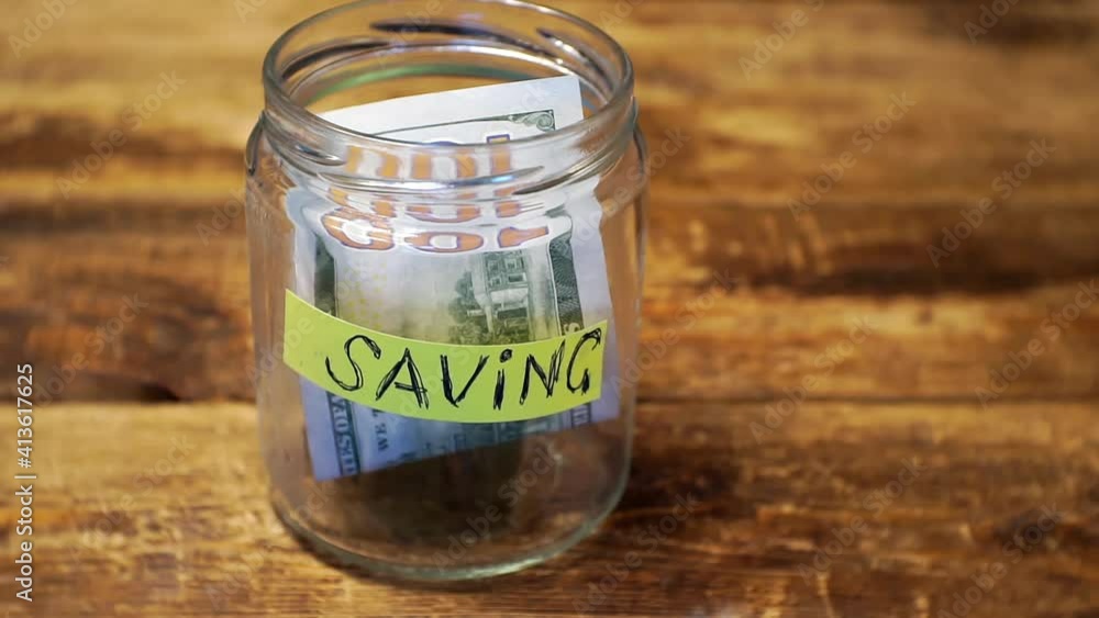 business concept.hand puts a few hundred dollar bills in a savings jar. business concept.hand puts a few hundred dollar bills in a savings jar.