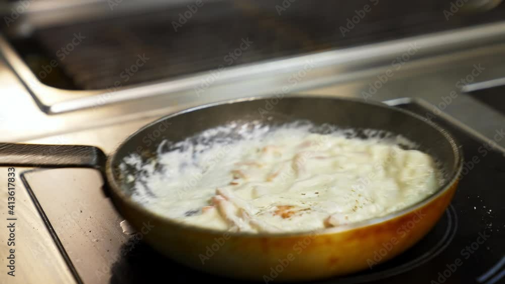 Cooking delicious meal in white sauce. Chef is cooking tasty dish in a frying pan in a restaurant. Close-up. Cooking delicious meal in white sauce. Chef is cooking tasty dish in a frying pan in a restaurant. Close-up.