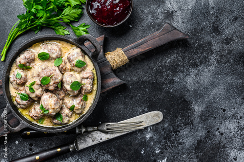 Beef meatballs in cream sauce in a frying pan. Black background. Top view. Copy space