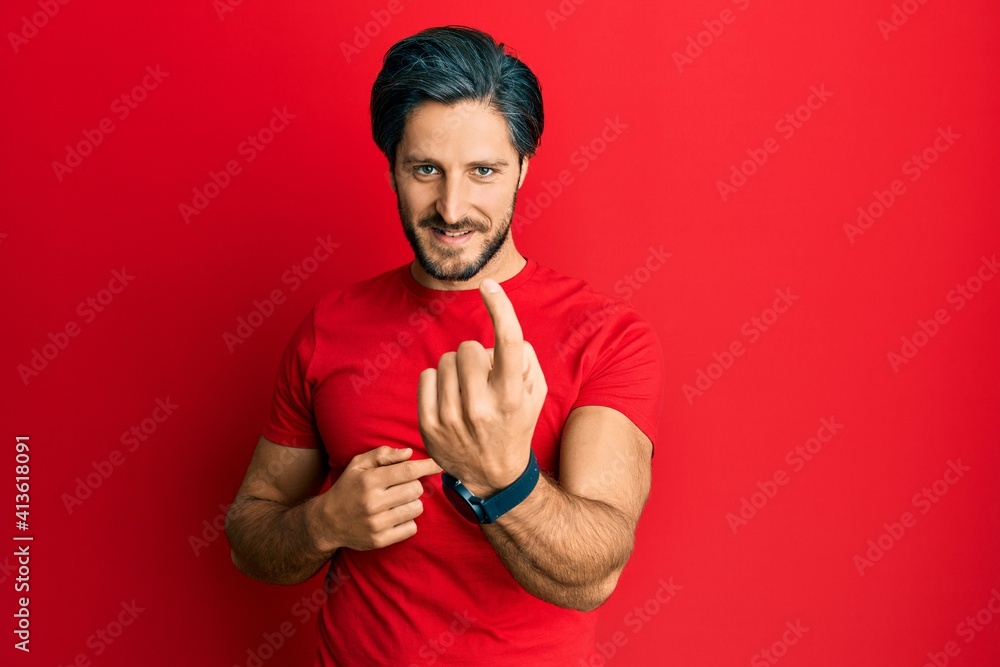 Young hispanic man wearing casual red t shirt beckoning come here gesture with hand inviting welcoming happy and smiling Young hispanic man wearing casual red t shirt beckoning come here gesture with hand inviting welcoming happy and smiling