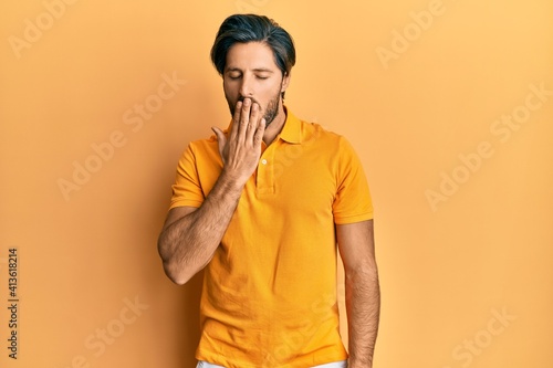 Young hispanic man wearing casual yellow t shirt bored yawning tired covering mouth with hand. restless and sleepiness. © Krakenimages.com