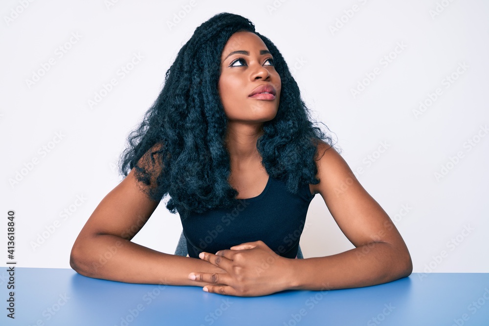 Beautiful african woman wearing casual clothes sitting on the table looking to side, relax profile pose with natural face with confident smile. Beautiful african woman wearing casual clothes sitting on the table looking to side, relax profile pose with natural face with confident smile.