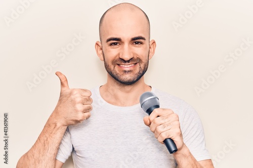 Young handsome bald man singing song using microphone smiling happy and positive, thumb up doing excellent and approval sign