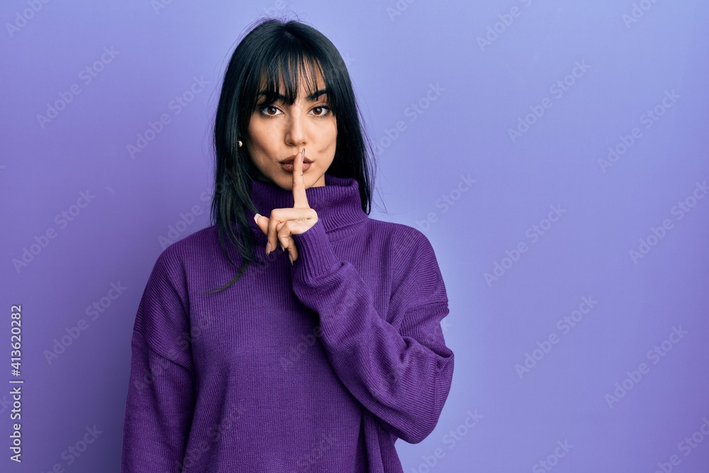 Young brunette woman with bangs wearing turtleneck sweater asking to be quiet with finger on lips. silence and secret concept.