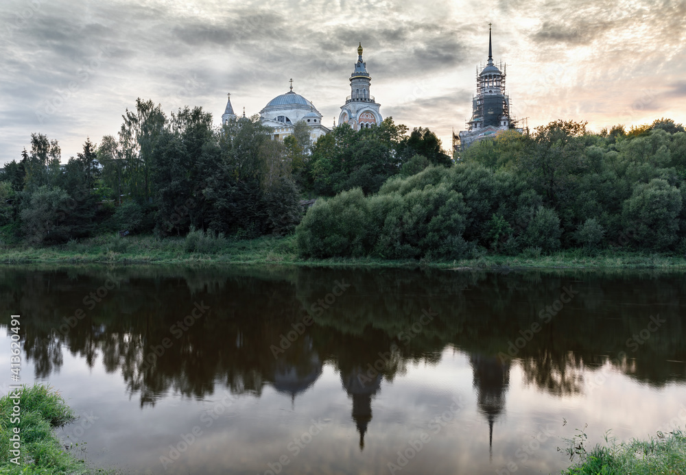 View of the Orthodox Cathedral on the river bank. Landscape with a view of the river, trees and reflection in the water in the evening light at sunset