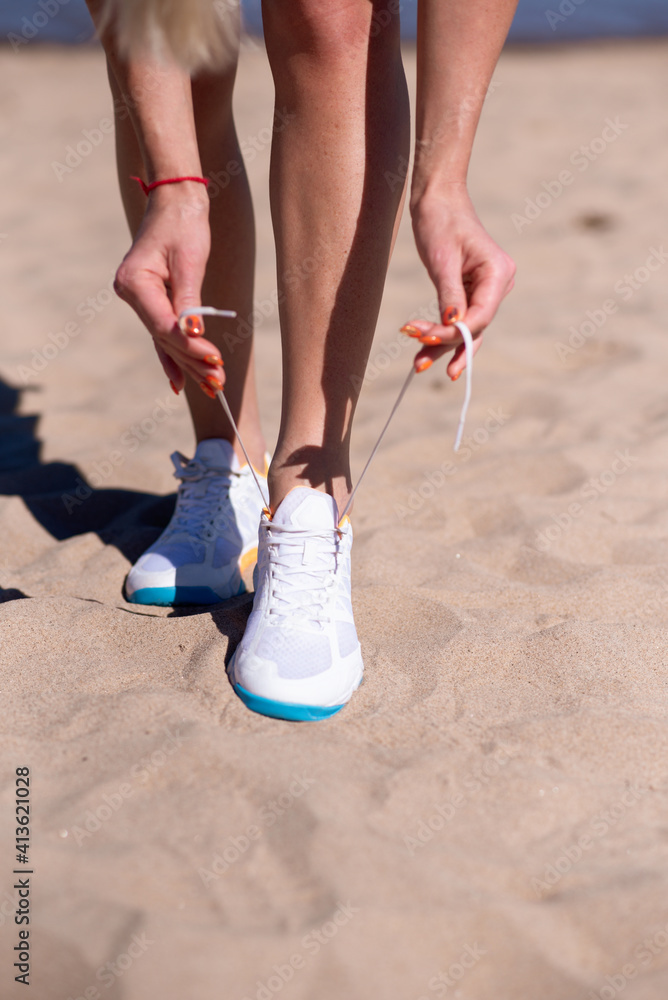 Legs of an athlete in sneakers sitting in a yoga pose. A woman is engaged in fitness on the beach. Sport and wellness concept.