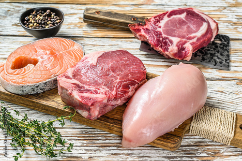 Fresh raw beef striploin steak, chicken breast fillet, pork and salmon steak. White wooden background. Top view
