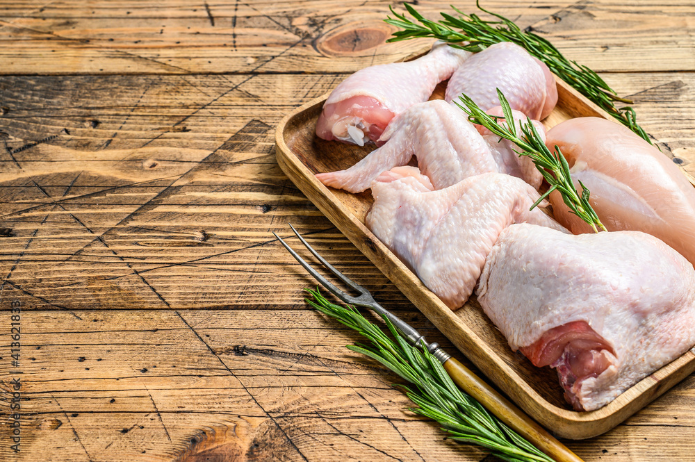 Fresh raw chicken meat, wings, breast, thigh and drumsticks on a wooden tray. Wooden background. Top view. Copy space - obrazy, fototapety, plakaty 