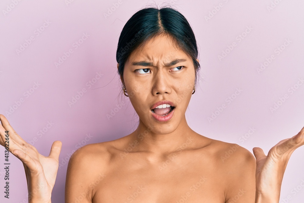 Young chinese woman standing topless showing skin crazy and mad shouting and yelling with aggressive expression and arms raised. frustration concept. Young chinese woman standing topless showing skin crazy and mad shouting and yelling with aggressive expression and arms raised. frustration concept.