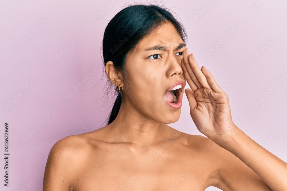 Young chinese woman standing topless showing skin shouting and screaming loud to side with hand on mouth. communication concept. Young chinese woman standing topless showing skin shouting and screaming loud to side with hand on mouth. communication concept.