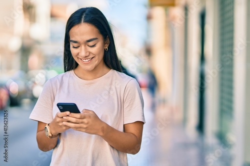 Young latin girl smiling happy using smartphone at the city.