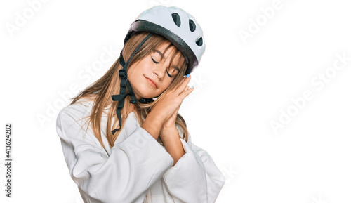 Teenager caucasian girl wearing bike helmet sleeping tired dreaming and posing with hands together while smiling with closed eyes.