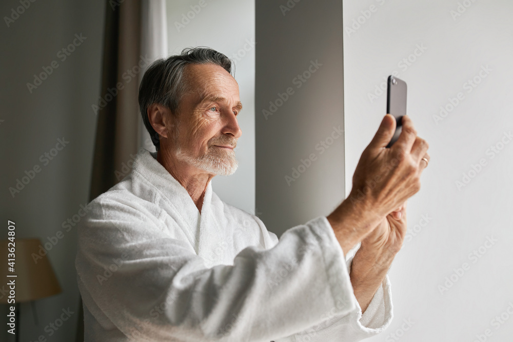 Senior man taking photographs on his smartphone from a hotel room Senior man taking photographs on his smartphone from a hotel room