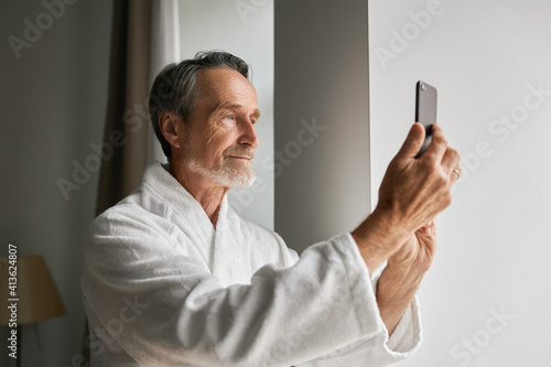 Senior man taking photographs  on his smartphone from a hotel room