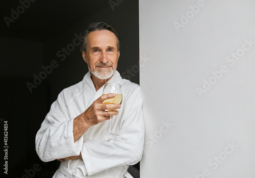 Portrait of a senior man leaning on a wall holding a glass of wine