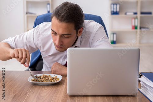 Hungry male employee eating buckwheat during break