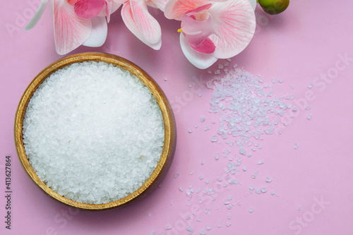Bath salt in a wooden bowl and with orchid flowers close-up, with blurred soft focus on a pink background, spa concept, baths, massage and relaxation, scrub and body care