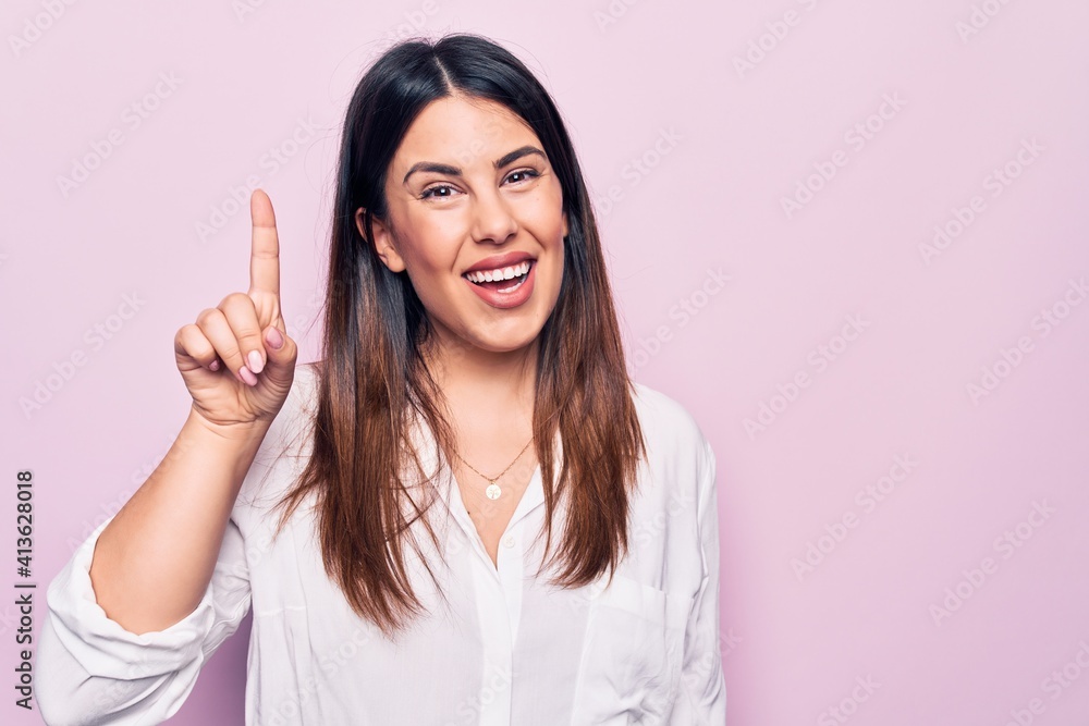 Young beautiful brunette woman wearing elegant shirt standing over isolated pink background smiling with an idea or question pointing finger up with happy face, number one Young beautiful brunette woman wearing elegant shirt standing over isolated pink background smiling with an idea or question pointing finger up with happy face, number one