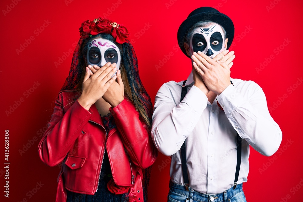 Couple wearing day of the dead costume over red shocked covering mouth with hands for mistake. secret concept. Couple wearing day of the dead costume over red shocked covering mouth with hands for mistake. secret concept.