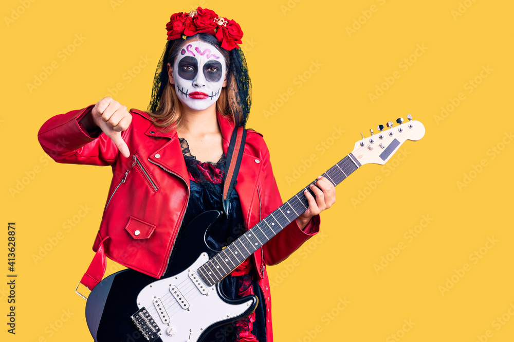 Woman wearing day of the dead costume playing electric guitar with angry face, negative sign showing dislike with thumbs down, rejection concept