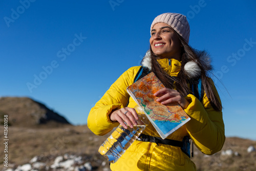 Portrait of a smiling woman hiking and holding a map at the top of the mountain. 
