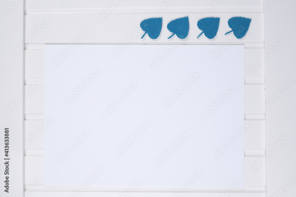 Kartka papieru biała na białym blacie drewnianym z listkami zielonymi - obrazy, fototapety, plakaty 