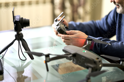  A man writes a blog in front of a camera about taking photos with a quadrocopter. He is holding the remote control from the drone. Selective focus.