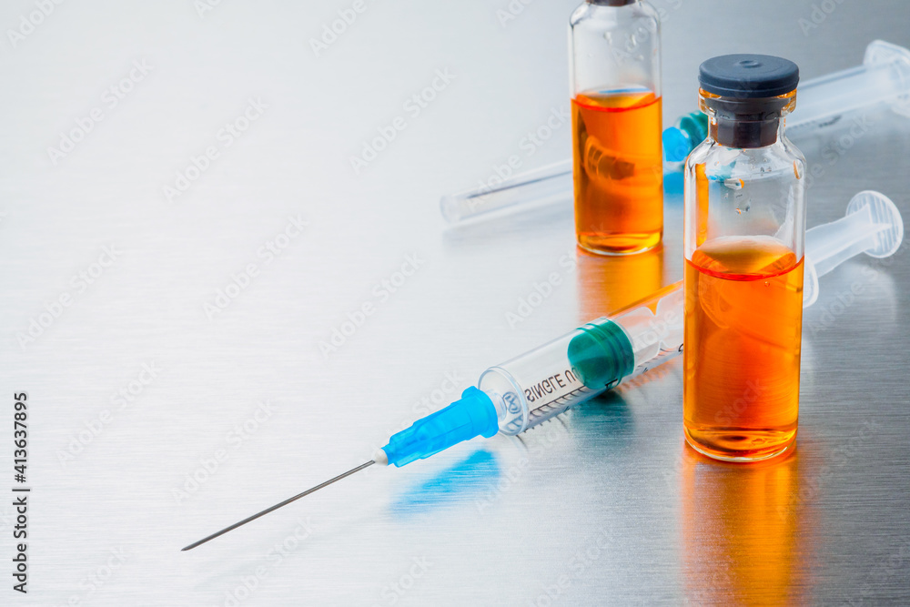 Selective focus. Close-up shot of injection syringes and ampoules with orange coronavirus vaccine on a silver aluminum background. Covid-19 pandemic medical concept. Copy space. Selective focus. Close-up shot of injection syringes and ampoules with orange coronavirus vaccine on a silver aluminum background. Covid-19 pandemic medical concept. Copy space.