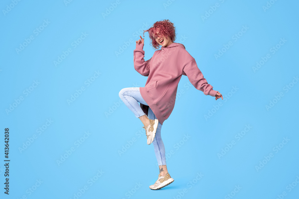Tattooed girl in jeans, hoodie and sneakers with colored curly pink hair dancing and having fun Tattooed girl in jeans, hoodie and sneakers with colored curly pink hair dancing and having fun