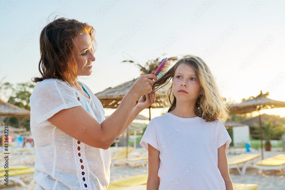 Family relaxing weekend on beach, mother combing hair of her preteen daughter Family relaxing weekend on beach, mother combing hair of her preteen daughter