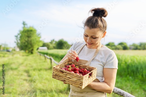 Smiling middle aged woman in apron with basket of strawberries on farm