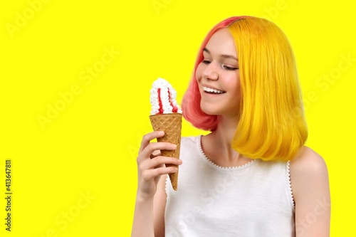 Smiling model teenager with ice cream in waffle cone over yellow background