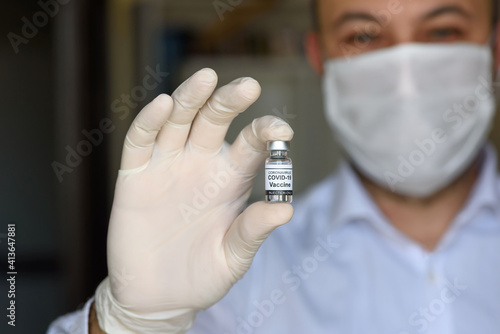Doctor with white gloves holds bottle with COVID-19 vaccine. Concept of medicine, clinical trial and treatment due to SARS-CoV-2 coronavirus. Blur concept