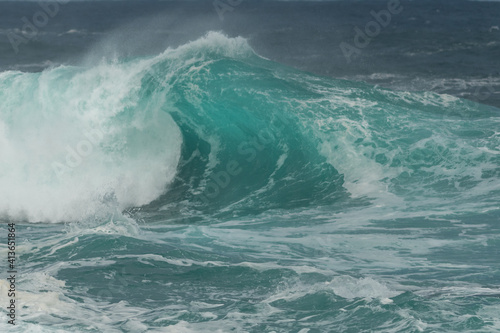 An angry turquoise green colour massive rip curl of a wave as it barrel rolls along the cold ocean. The white mist and froth from the wave are foamy and fluffy. 