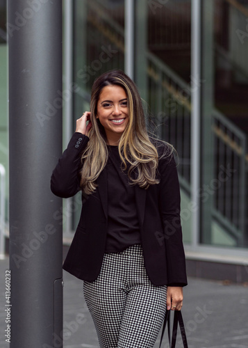 Young smiling successful business woman leaning on post in urban office