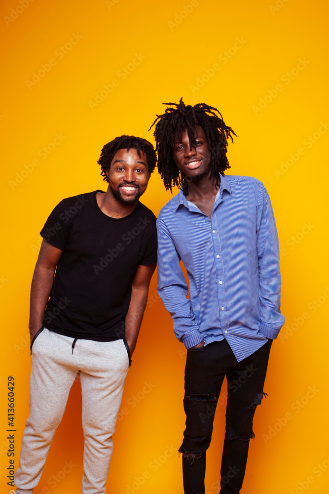 Obraz premium two african american guys posing cheerful together on yellow background, lifestyle people concept