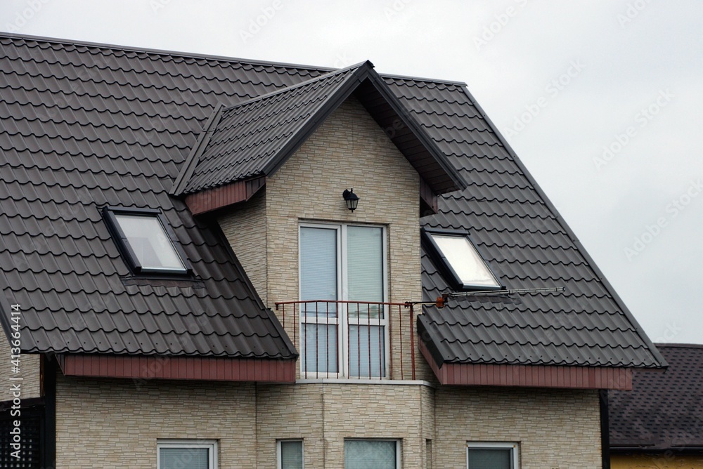 open iron balcony on the gray  brick wall of the house under the brown tiled roof against the sky