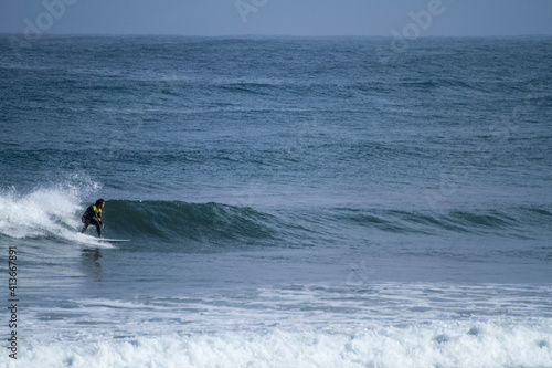 A surfer sportingly rides down a wave on a beach in Portugal on the Atlantic Ocean
