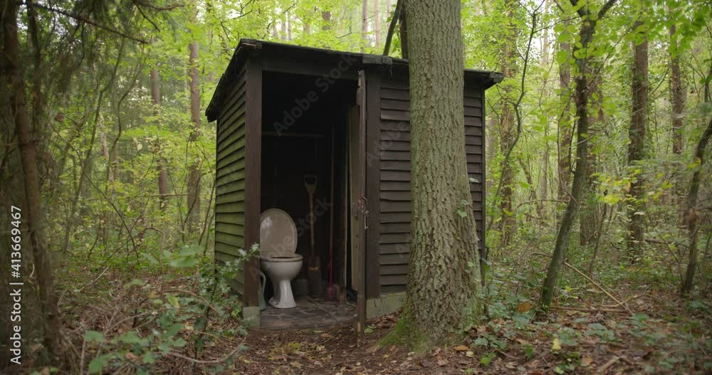 Shed with a toilet in the middle of the woods. Outside lavatory. Outside toilet in the forest. Old Shack with toilet bowl and gear. Primitive bathroom with open door in an outbuilding between trees. Shed with a toilet in the middle of the woods. Outside lavatory. Outside toilet in the forest. Old Shack with toilet bowl and gear. Primitive bathroom with open door in an outbuilding between trees.