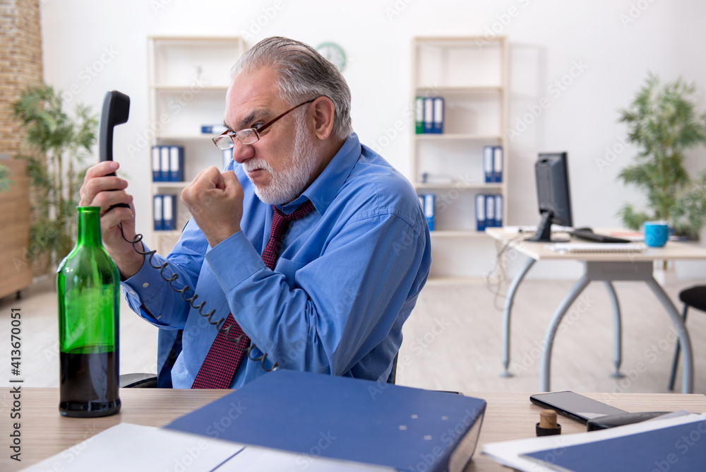 Old male employee drinking alcohol in the office Old male employee drinking alcohol in the office